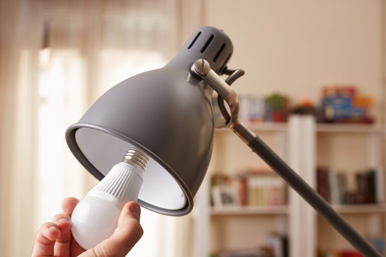 Mão trocando uma lâmpada comum por LED em casa